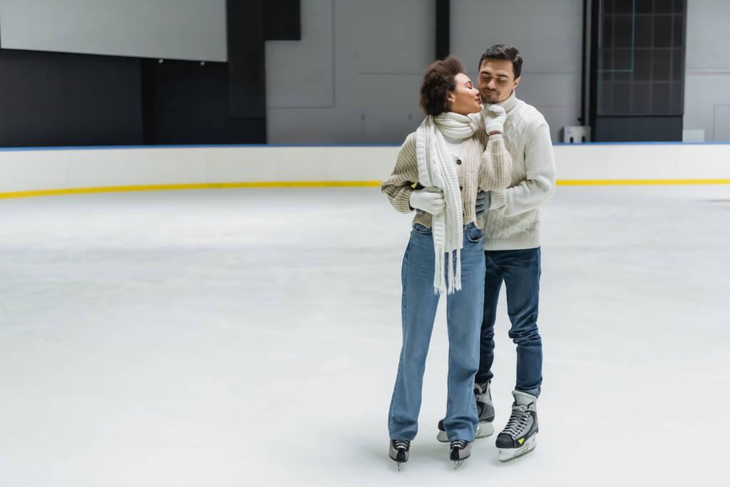 Junge Afroamerikanerin küsst Freund in warmer Kleidung auf Eisbahn  - Foto, Bild