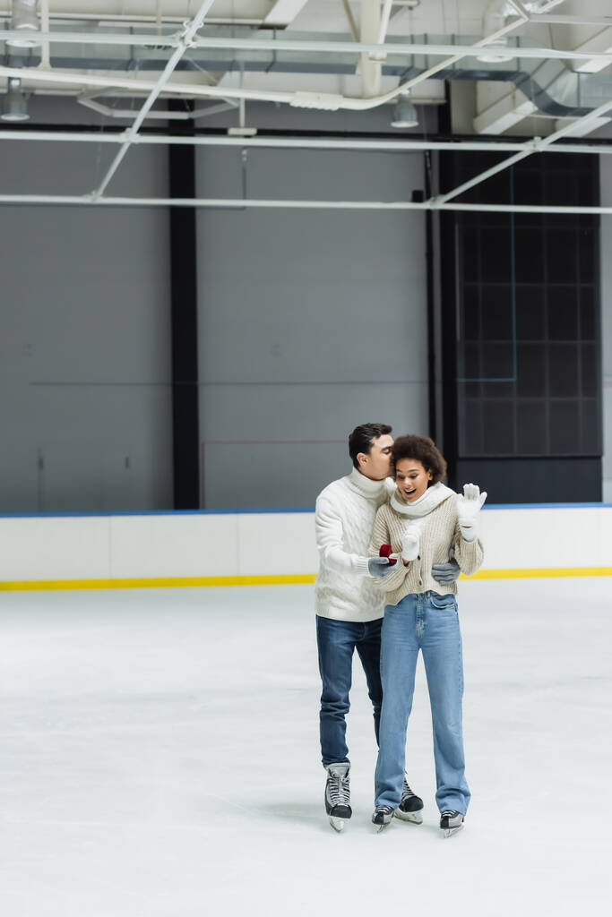Man hugging african american girlfriend and holding engagement ring on ice rink  - Photo, Image