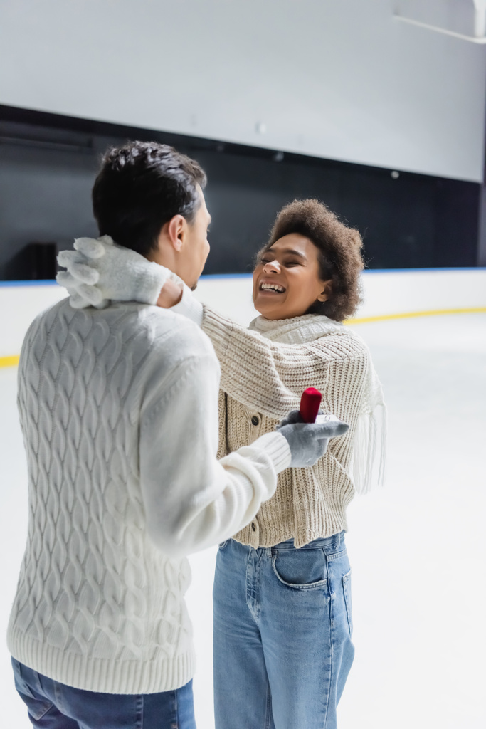 Feliz mulher afro-americana abraçando namorado com anel de proposta na pista de gelo  - Foto, Imagem