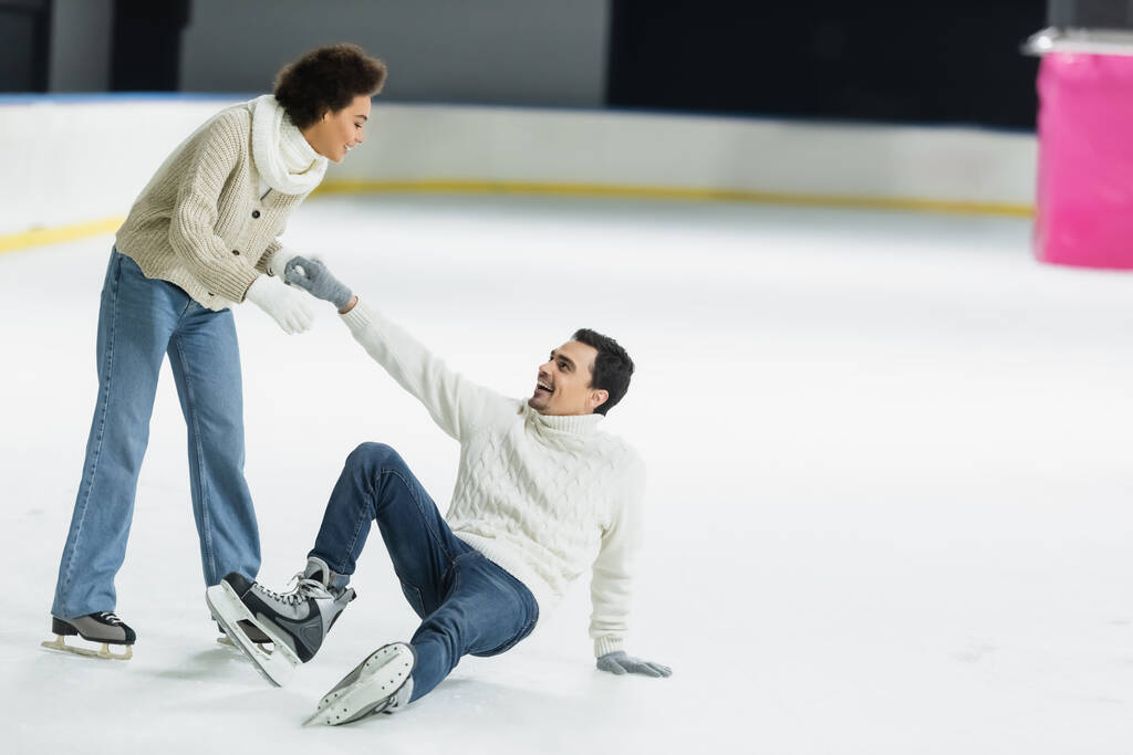 Smiling african american woman helping boyfriend falling on ice rink  - Photo, Image