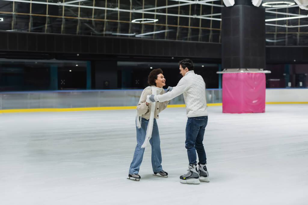 Cheerful african american woman holding hands of boyfriend while having fun on ice rink  - Photo, Image