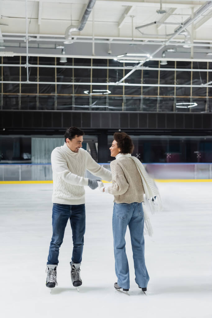 Pozitív többnemzetiségű pár fogja egymás kezét korcsolyázás közben a jégpályán a dátum alatt - Fotó, kép