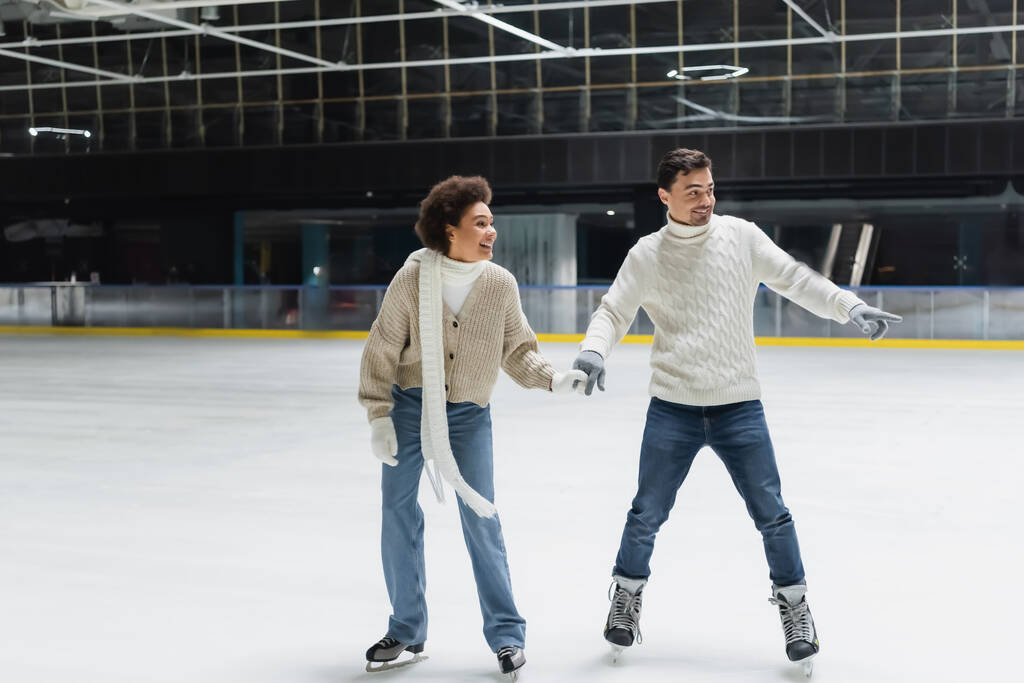 Jeune homme pointant du doigt et patinage sur glace avec une petite amie afro-américaine sur la patinoire  - Photo, image