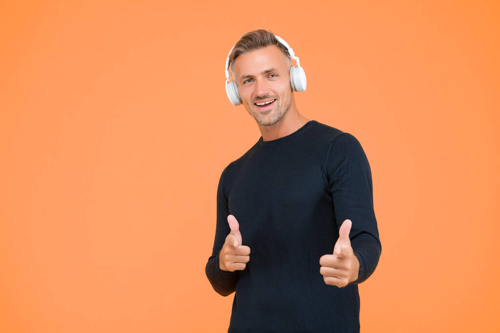 pohledný veselý muž poslouchat hudbu ve stylových sluchátkách na žlutém pozadí ukazující prst, baví. - Fotografie, Obrázek