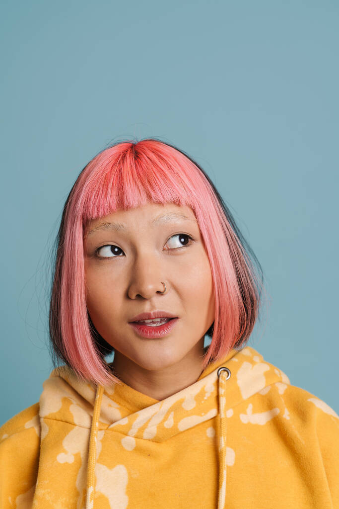 Aasian tyttö vaaleanpunaiset hiukset ja lävistykset poseeraa samalla syrjään eristetty yli sininen tausta - Valokuva, kuva