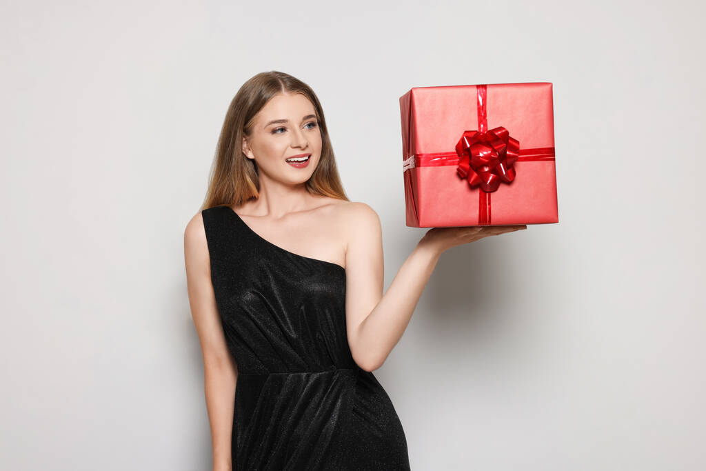 Portrét krásné mladé ženy v elegantních černých šatech s červenou dárkovou krabicí na bílém pozadí - Fotografie, Obrázek