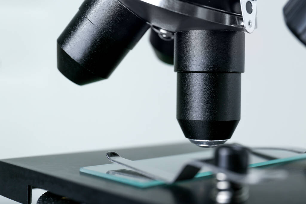 Σύγχρονο ιατρικό μικροσκόπιο με γυάλινη διαφάνεια σε γκρι φόντο, closeup - Φωτογραφία, εικόνα