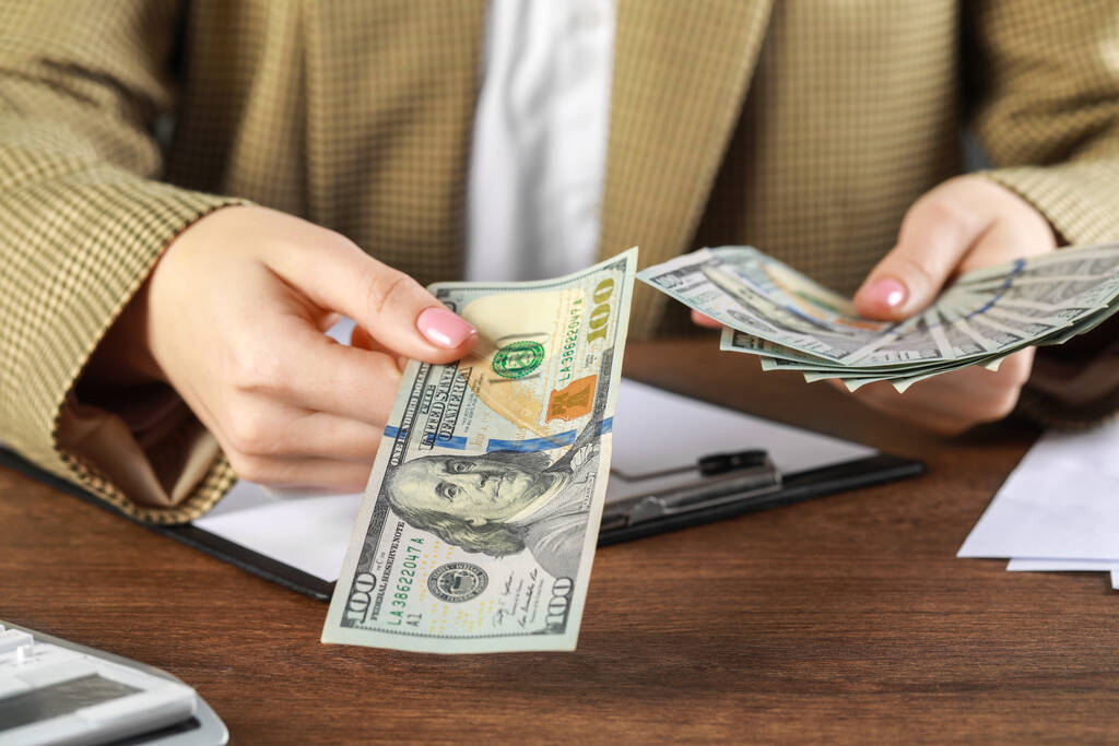 Žena držící dolarové bankovky u dřevěného stolu, detailní záběr. Koncept směny peněz - Fotografie, Obrázek