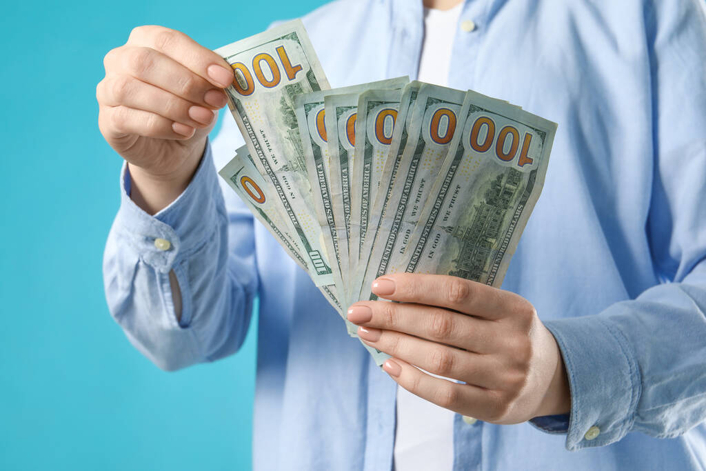 Vrouw die dollarbiljetten telt op turquoise achtergrond, close-up. Geldwisselingsconcept - Foto, afbeelding