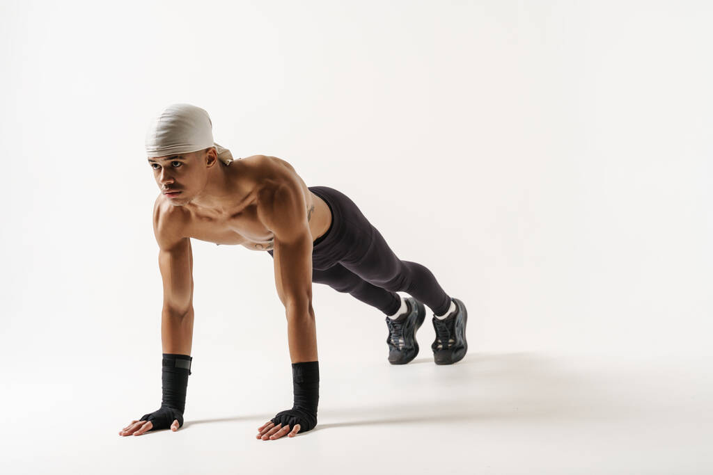 Young shirtless sportsman doing exercise while working out isolated over white background - Photo, Image