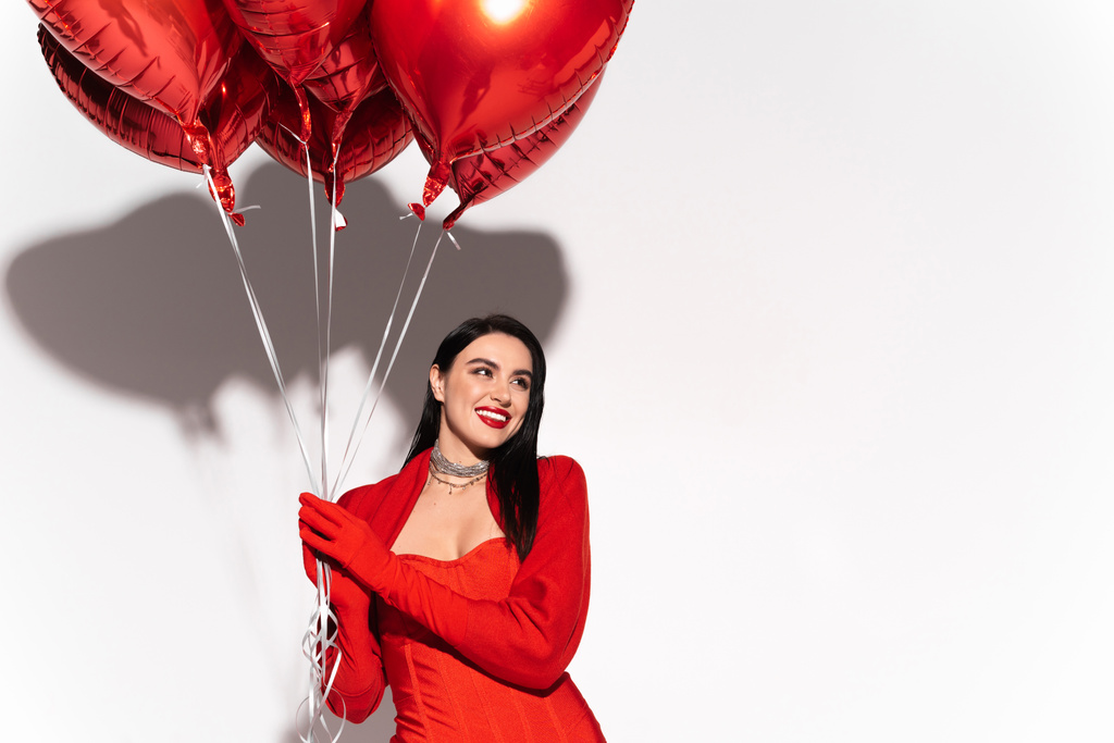 Kırmızı dudaklı, gülümseyen kadın beyaz arka planda kalp şeklinde balonlar tutuyor.  - Fotoğraf, Görsel