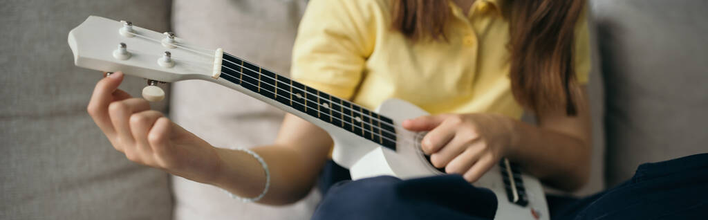 vue recadrée de l'enfant flou accordant la petite guitare hawaïenne à la maison, bannière - Photo, image