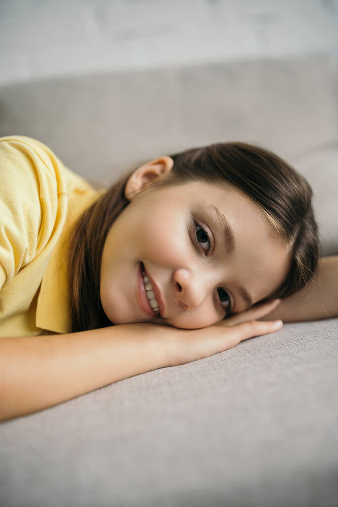 feliz preadolescente chica acostada en un sofá suave y mirando a la cámara - Foto, Imagen