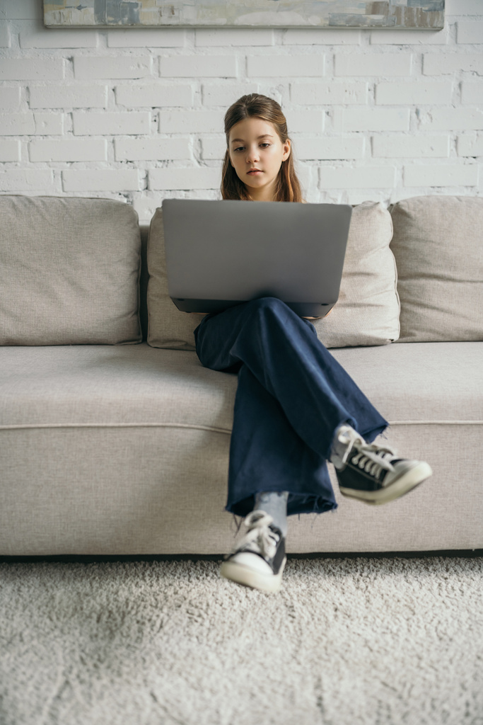 preteen κορίτσι με φορητό υπολογιστή κάθεται σε μοντέρνο άνετο καναπέ στο σπίτι - Φωτογραφία, εικόνα