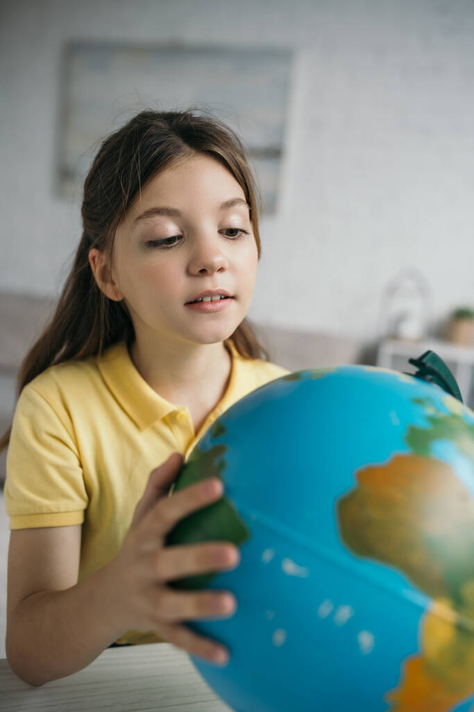 preteen schoolgirl looking at blurred globe and learning geography at home - Photo, Image