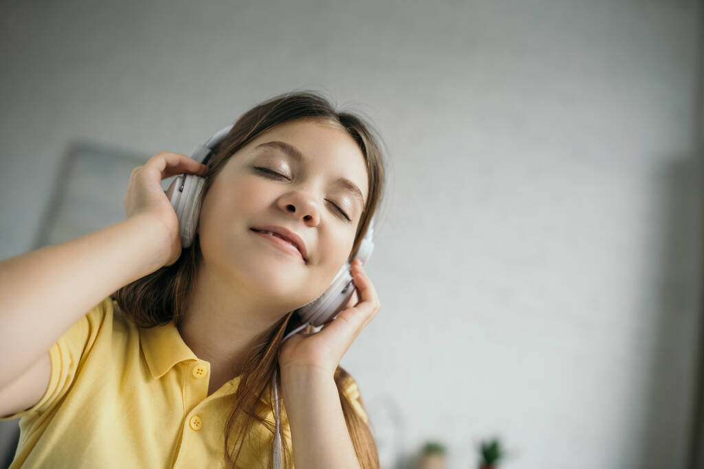laag gezichtspunt van tevreden tiener meisje met gesloten ogen luisteren muziek in hoofdtelefoon - Foto, afbeelding