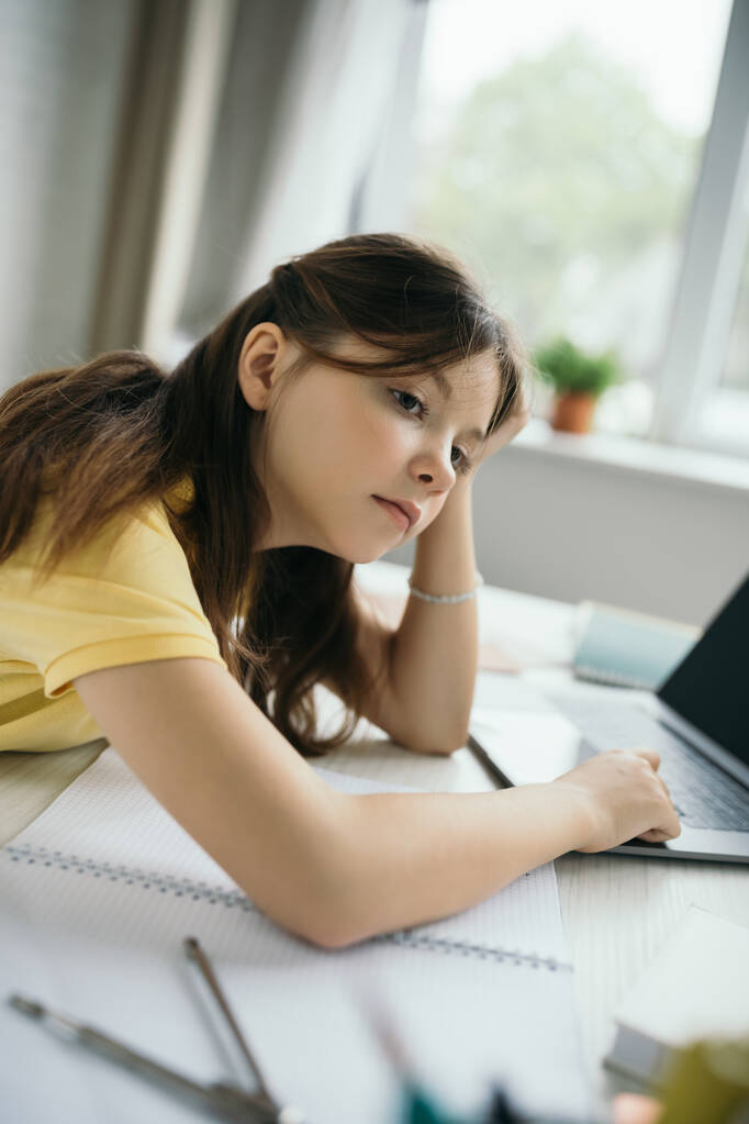 thoughtful and bored girl sitting near notebook and blurred laptop at home - Photo, Image