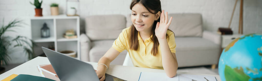 örömteli lány nézi laptop és integető kéz alatt online lecke otthon, banner - Fotó, kép