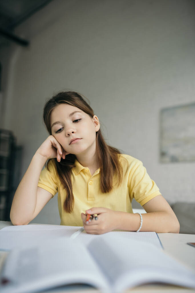 задумчивая и уставшая девушка держит ручки, сидя с рукой возле лица дома - Фото, изображение