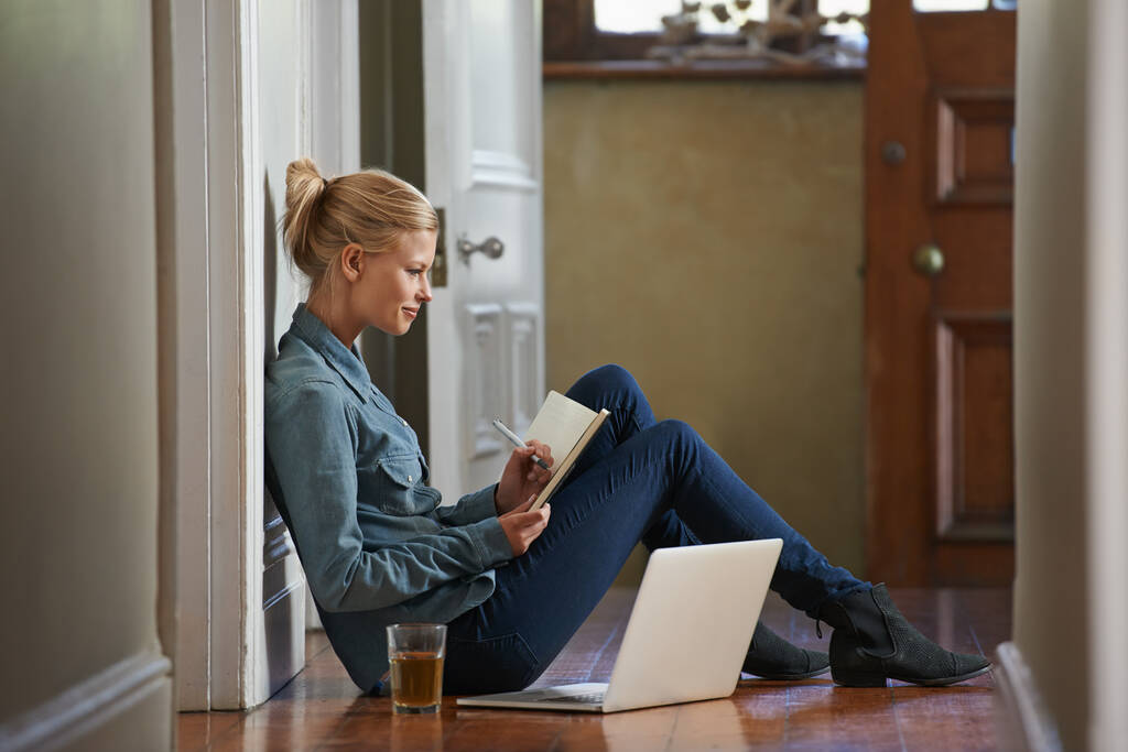 Записываю несколько идей. Молодая женщина, сидящая на полу и исследующая ноутбук - Фото, изображение