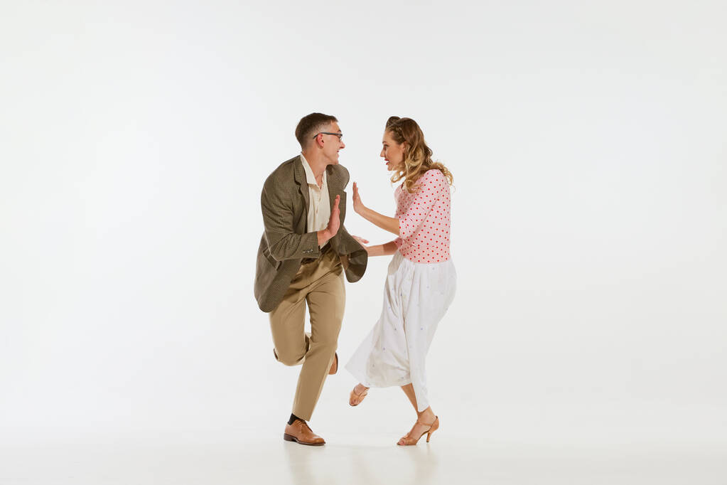 Amor en movimiento. Joven emocionado hombre y mujer que lleva ropa de estilo americano de los años 60 bailando danza retro aislada sobre fondo blanco. Música, energía, felicidad, humor, acción - Foto, imagen