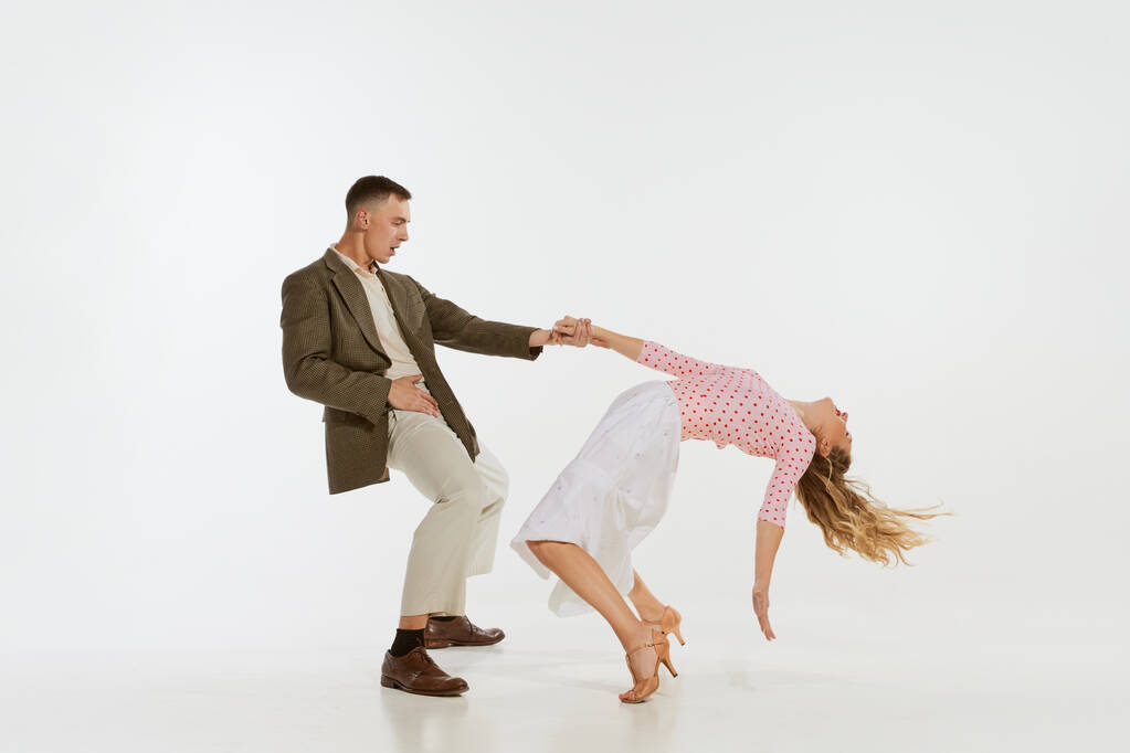 Amor em movimento. Jovem animado homem e mulher vestindo roupas de moda americana dos anos 60 dançando dança retro isolado em fundo branco. Música, energia, felicidade, humor, ação - Foto, Imagem