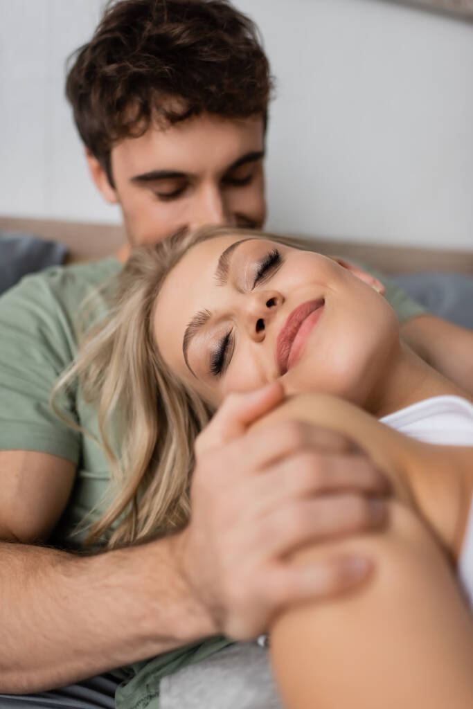 Homályos férfi ölelkezik vidám szőke barátnő az ágyban reggel  - Fotó, kép