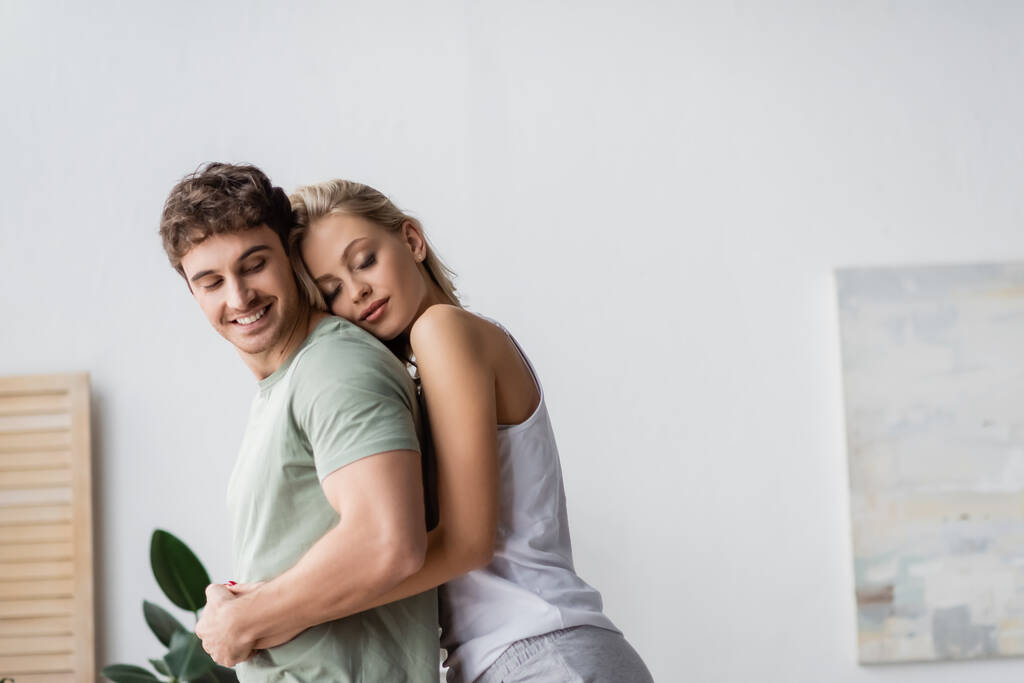 Blondi nainen pyjamassa syleilee hymyilevä poikaystävä kotona  - Valokuva, kuva