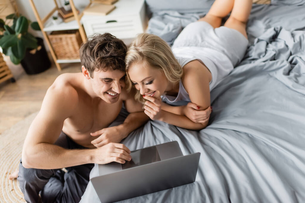Korkea kulma näkymä iloinen seksikäs pari katsomassa elokuvan laptop sängyssä  - Valokuva, kuva