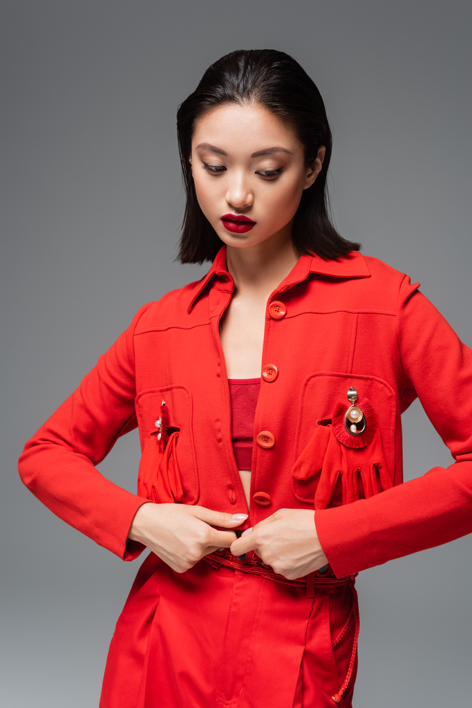 fiatal ázsiai nő piros kabátban díszített melltűk és kesztyűk elszigetelt szürke - Fotó, kép