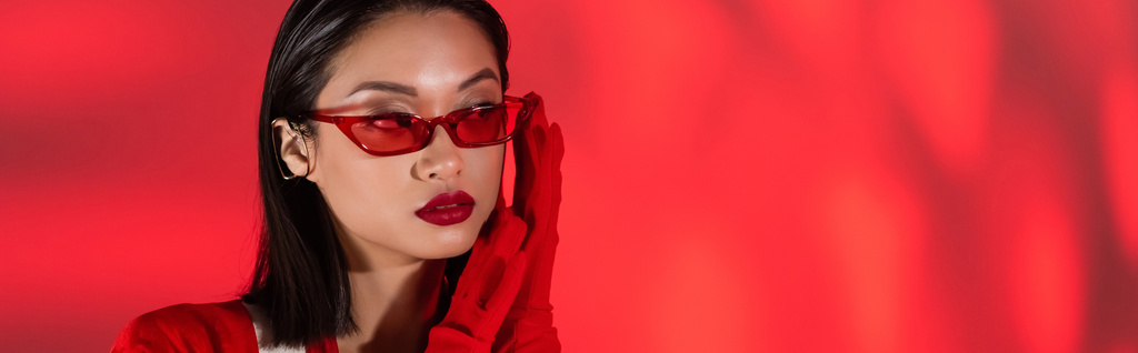 портрет азиатки в модных солнцезащитных очках и перчатках на красном абстрактном фоне, баннер - Фото, изображение