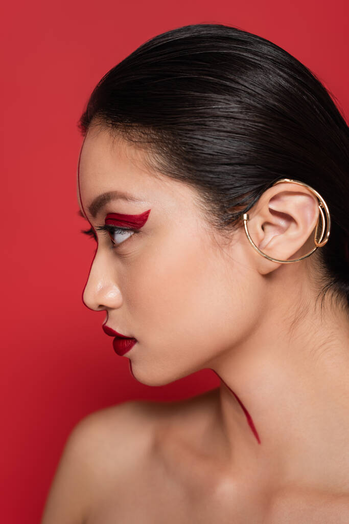 профиль брюнетки азиатской женщины с творческим обликом и ушной манжеты изолированы на красный цвет - Фото, изображение