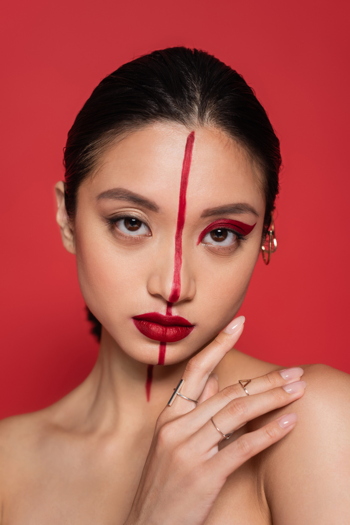 портрет брюнетки азіатки з рукою біля обличчя і творчий погляд, дивлячись на камеру ізольовано на червоному
 - Фото, зображення