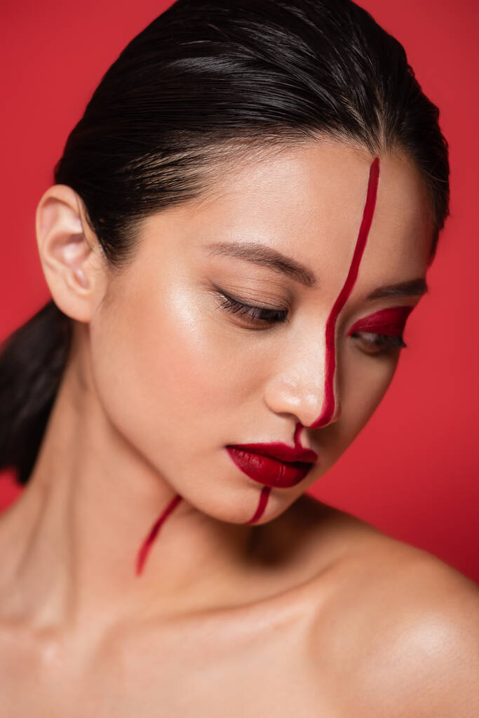 portrait of brunette asian woman with creative visage and naked shoulder posing isolated on red - Photo, Image