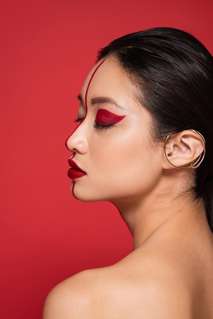 profil azjatyckiej kobiety z zamkniętymi oczami i makijażem artystycznym na perfekcyjnej twarzy odizolowanej na czerwono - Zdjęcie, obraz