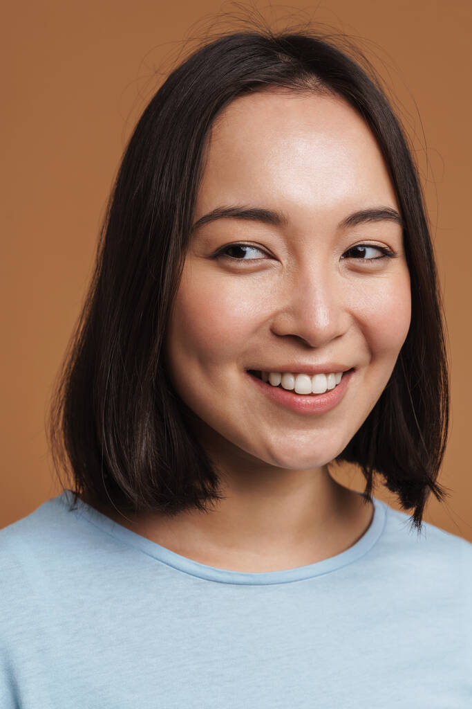 Joven mujer asiática usando camiseta riendo y mirando a un lado aislado sobre fondo beige - Foto, Imagen