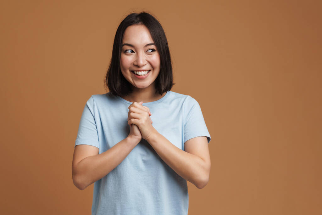 Joven mujer asiática riendo y tomándose de la mano aislada sobre fondo beige - Foto, imagen