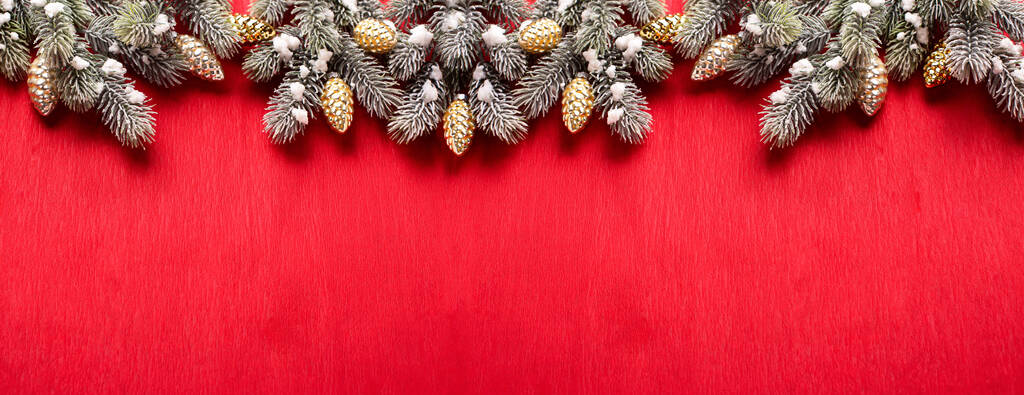 Длинный заказ от ветвей елки и декоративных золотых конусов на текстурированном фоне из красной бумаги. Вид сверху. Рождество, новогодние праздники. Место для текста. - Фото, изображение