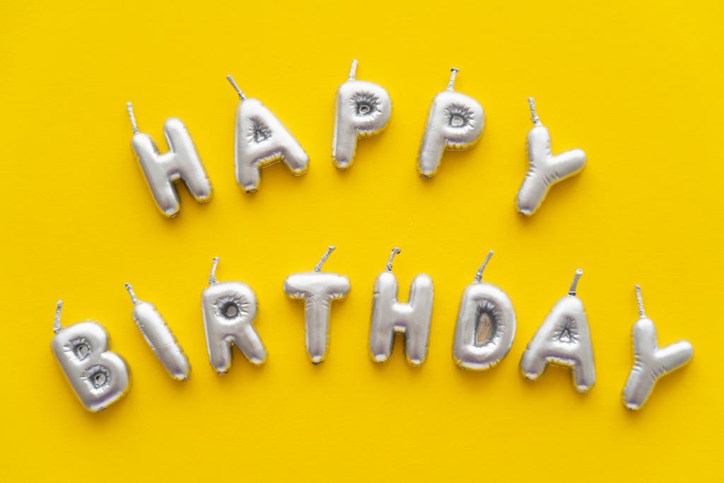 Верхний вид праздничных свечей в форме надписи "С днем рождения" на желтом фоне  - Фото, изображение