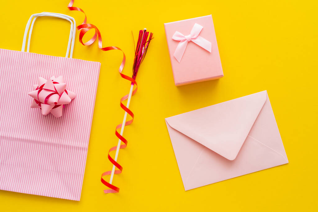 Vista superior do envelope rosa perto do presente e saco de compras no fundo amarelo  - Foto, Imagem