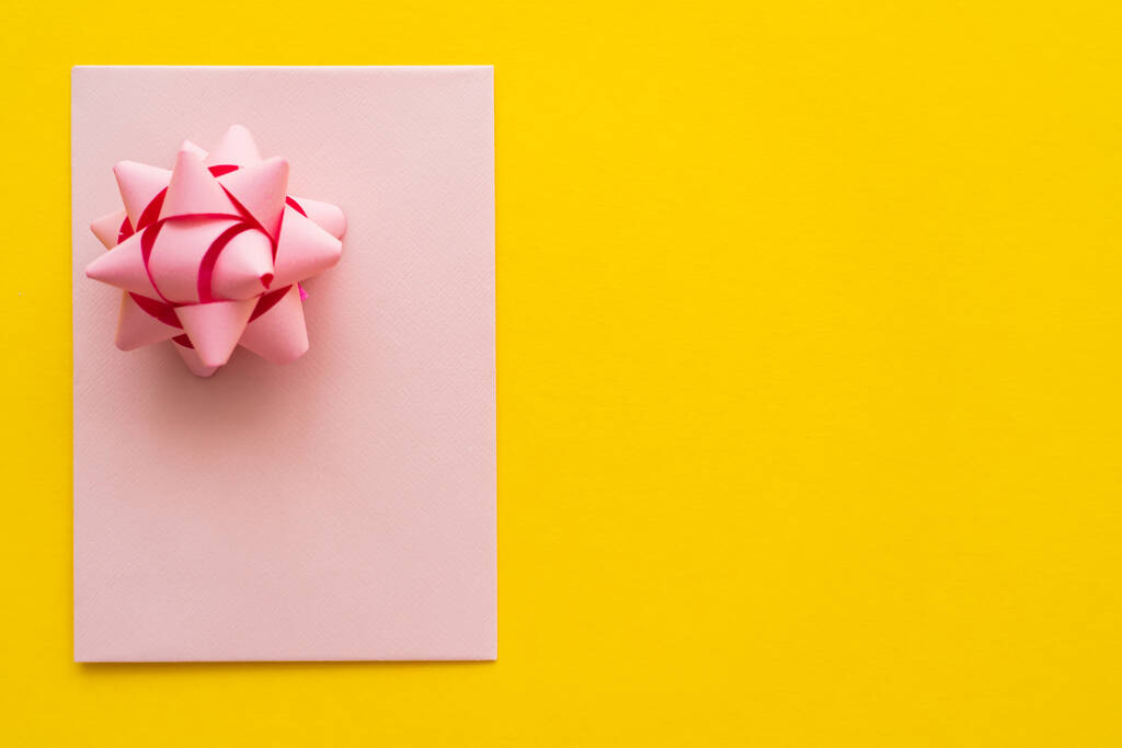 Top άποψη του ροζ ευχετήρια κάρτα με τόξο δώρο σε κίτρινο φόντο με αντίγραφο χώρου  - Φωτογραφία, εικόνα