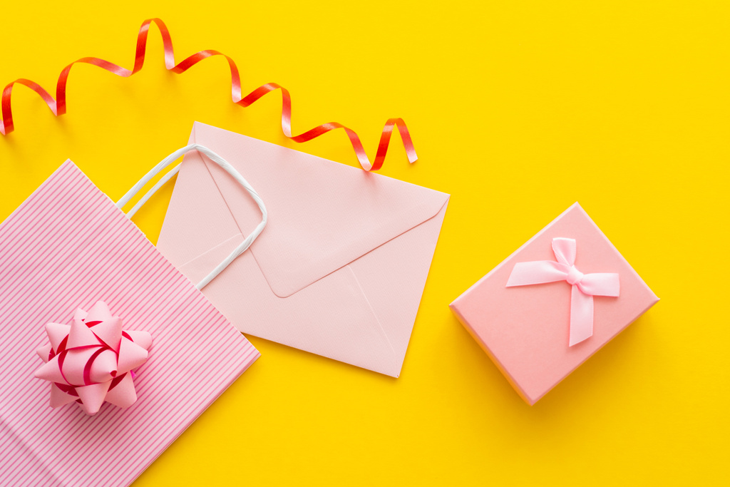 Draufsicht auf rosa Einkaufstasche in der Nähe von Umschlag und Geschenk auf gelbem Hintergrund  - Foto, Bild