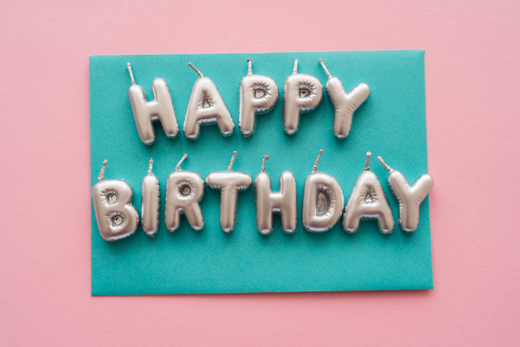 Вид сверху на свечи в форме поздравления с днем рождения на открытке на розовом фоне  - Фото, изображение