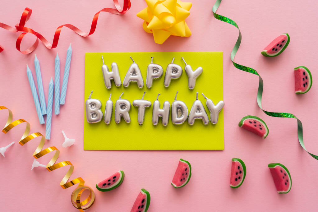 Vista superior de las velas en forma de letras de Feliz Cumpleaños cerca de dulces y serpentina sobre fondo rosa  - Foto, imagen