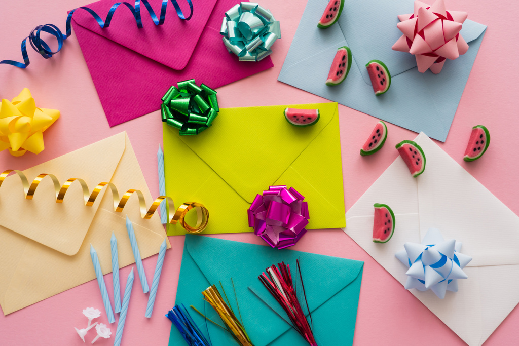 Vista superior de envelopes coloridos perto de doces e serpentina em fundo rosa  - Foto, Imagem