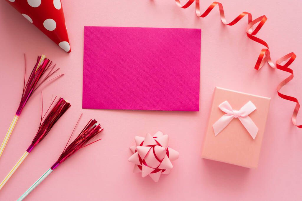 Widok z góry różowej kartki okolicznościowej obok pudełka z prezentami i serpentyny na różowym tle  - Zdjęcie, obraz
