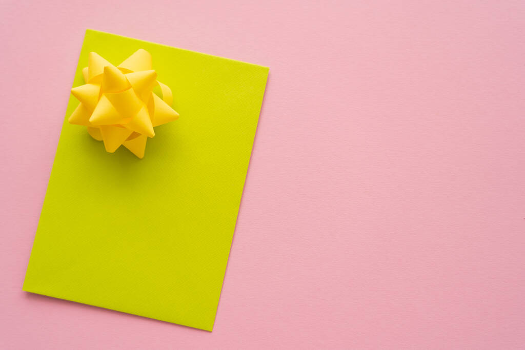 Vista superior de la tarjeta de felicitación vacía amarilla y el arco de regalo sobre fondo rosa  - Foto, Imagen