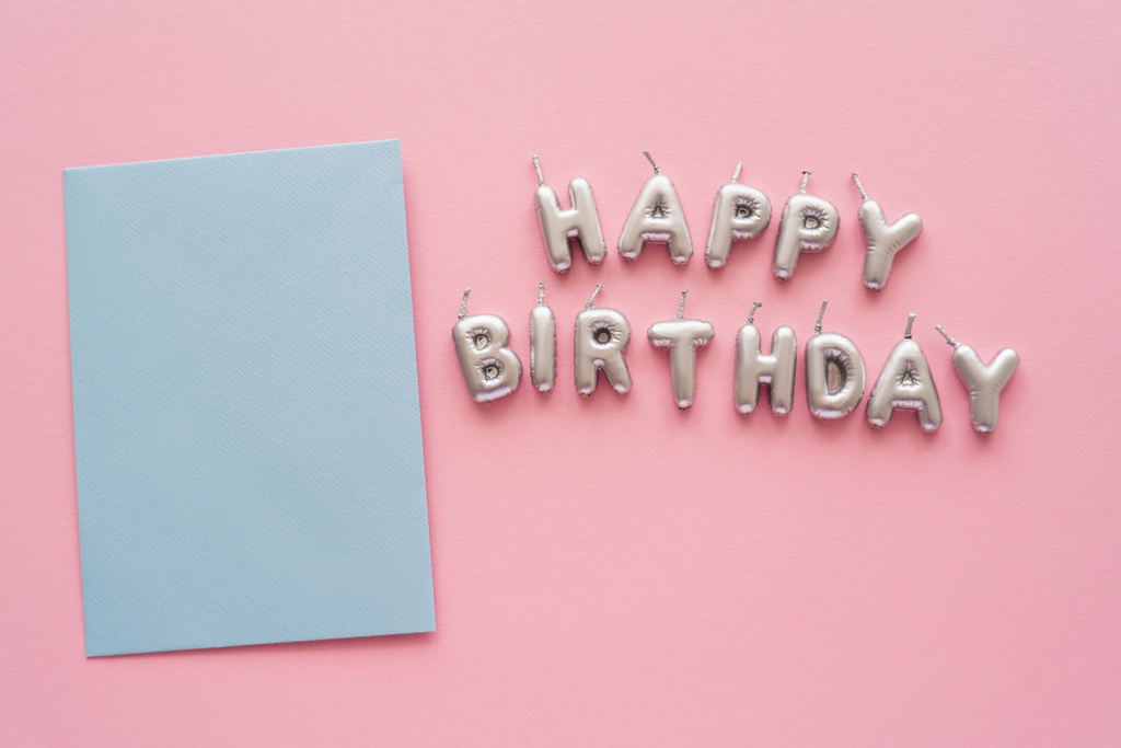 Вид на поздравительные открытки возле свечей в форме надписи "С днем рождения" на розовом фоне  - Фото, изображение