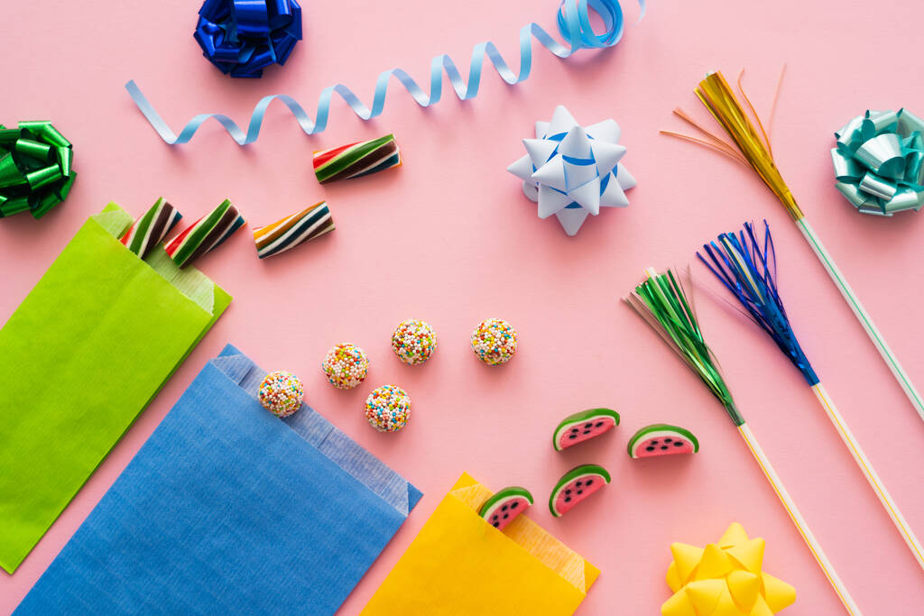 Вид сверху сладких конфет рядом с соломинками и подарочными киосками на розовом фоне  - Фото, изображение