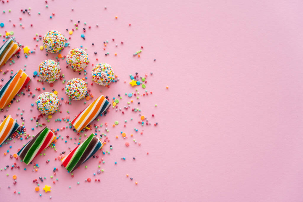 Draufsicht auf verschiedene bunte Süßigkeiten und Streusel auf rosa Hintergrund mit Kopierraum  - Foto, Bild